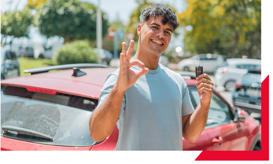 Joven sonriente mostrando las llaves de un auto rojo y haciendo señal de aprobación, representando importar carro sin titulo