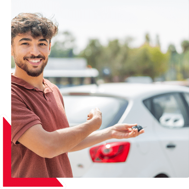 Joven sonriente mostrando las llaves de un auto blanco en estacionamiento, representando importar vehiculos a Mexico